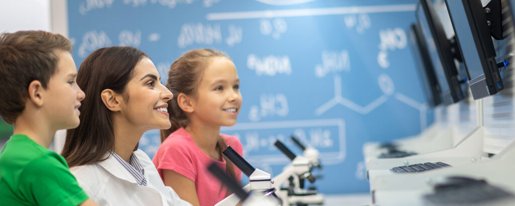 Teacher and pupils engaged in a science lesson using microscopes and digital tools.